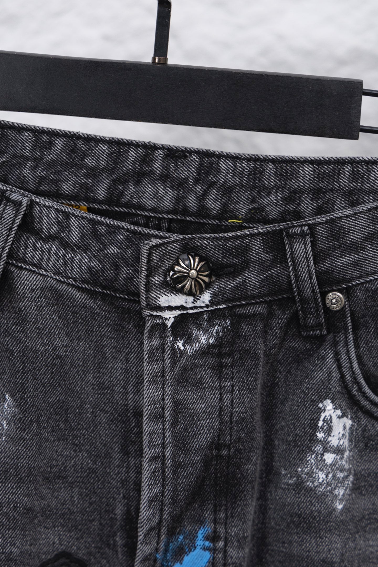Close-up of black denim pants button and waistband with decorative metal emblem; zipper side.