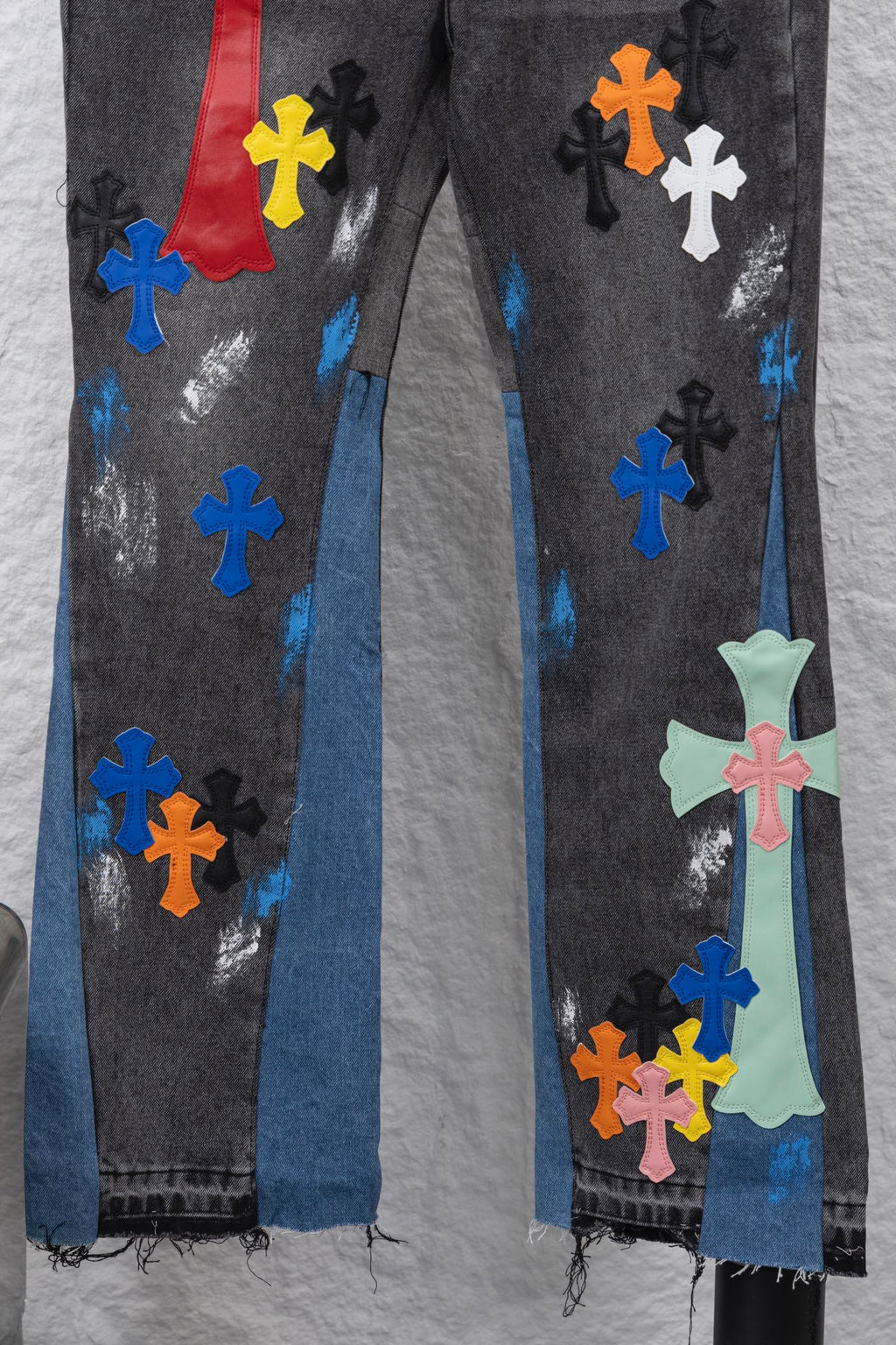 Close-up of black denim pants with multicolor cross patches and distressed blue areas.