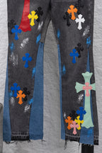 Close-up of black denim pants with multicolor cross patches and distressed blue areas.