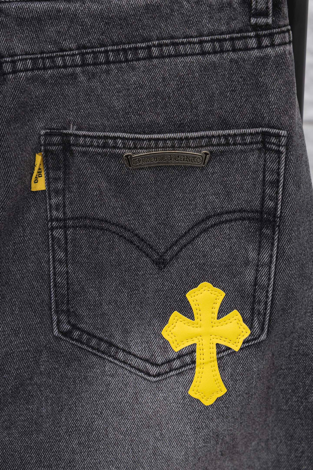 Dark denim pants, front pocket with yellow cross patch and small side tag