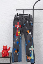 Black denim pants with multicolor cross patches and distressed blue panel inserts.