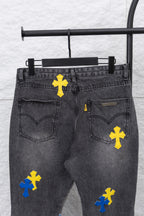 Black denim pants with yellow and blue cross patches; heart-shaped back pocket detail.