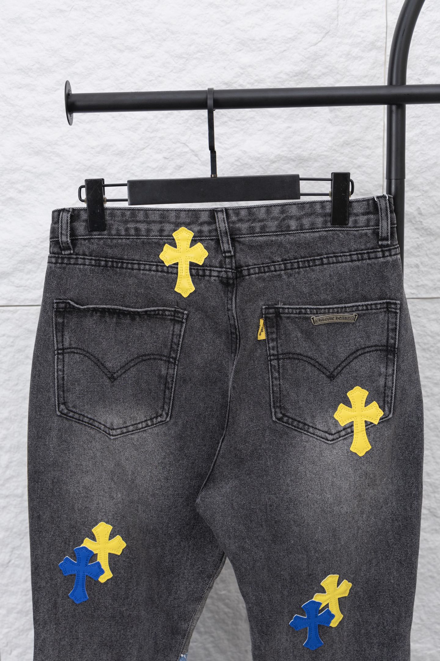 Black denim pants with yellow and blue cross patches; heart-shaped back pocket detail.
