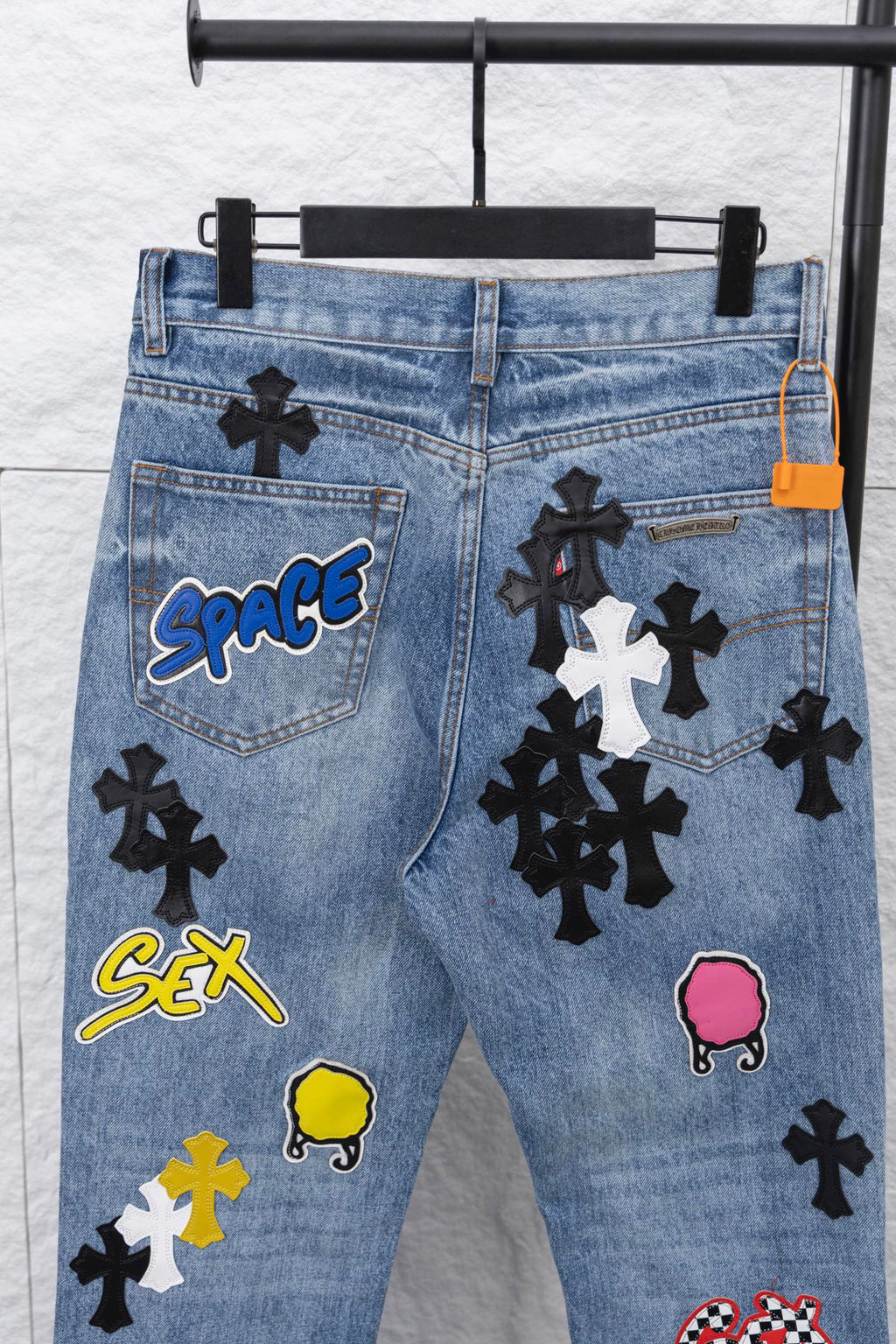 Light blue denim pants with pocket graphic patches, close-up front.