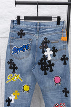 Light blue denim pants with pocket graphic patches, close-up front.