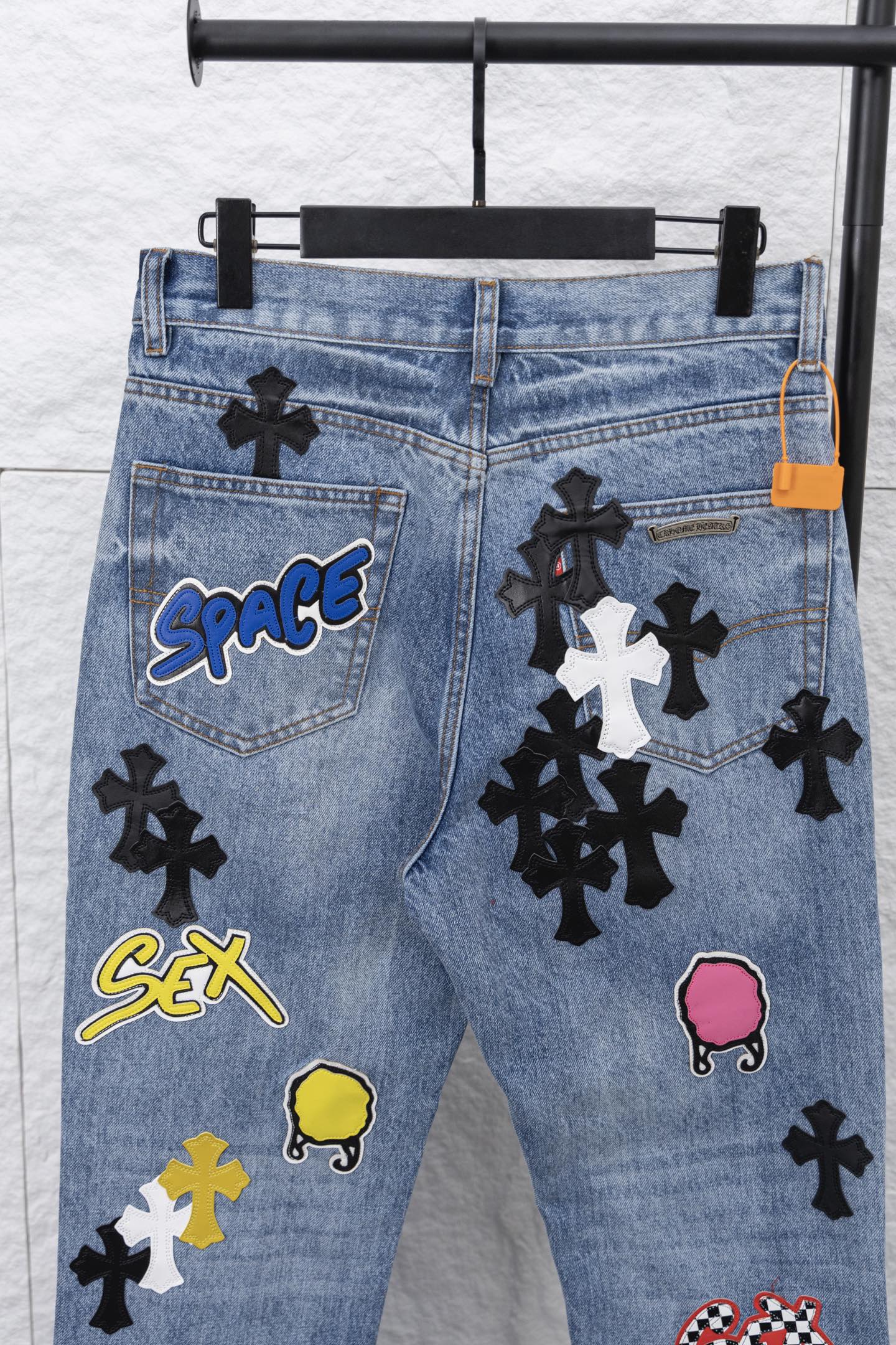 Light blue denim pants with pocket graphic patches, close-up front.