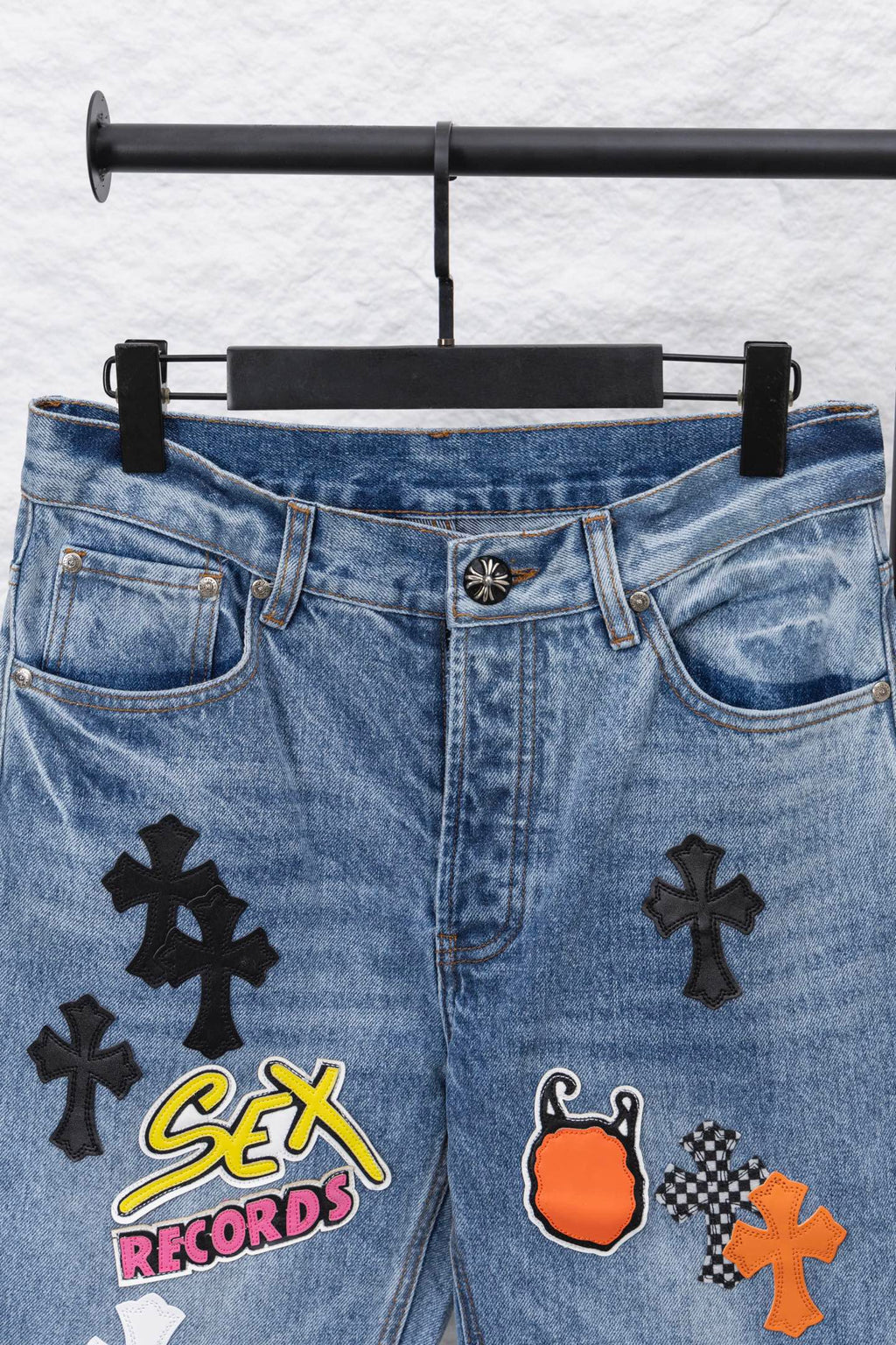 Light blue denim pants with front graphic patches, waistband view.