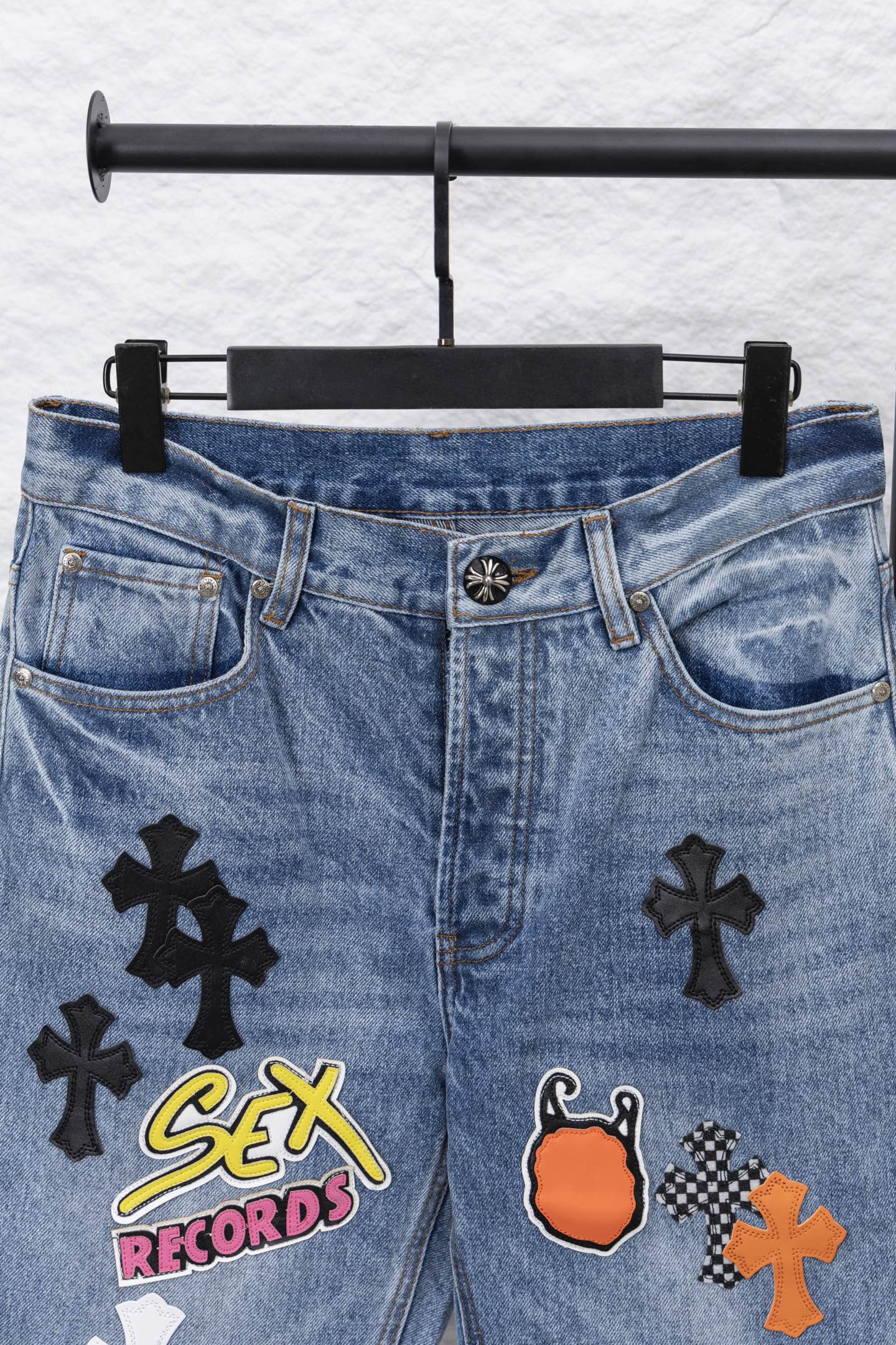 Light blue denim pants with front graphic patches, waistband view.