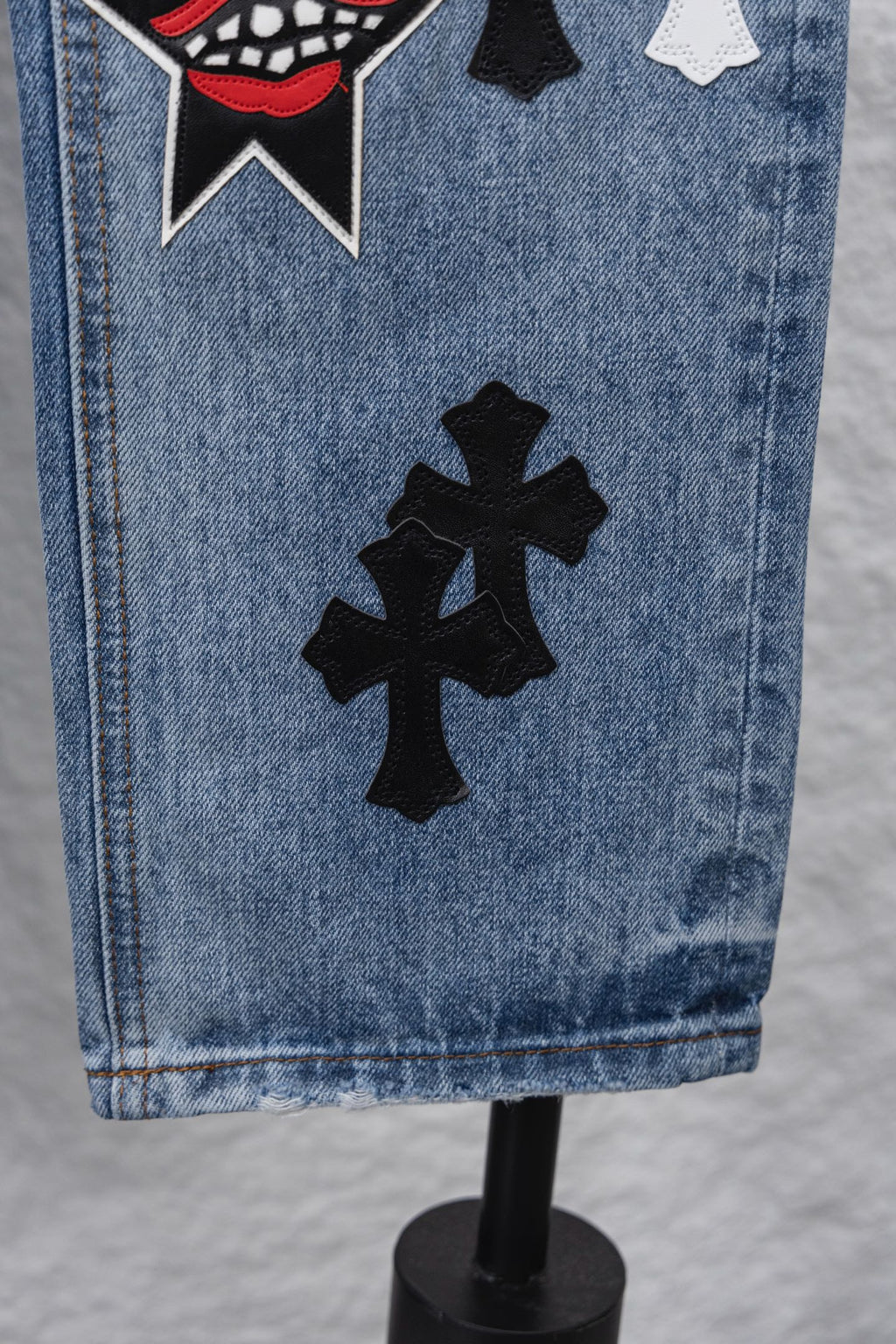 Light blue denim pants hem with large black cross patch, close-up.