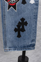 Light blue denim pants hem with large black cross patch, close-up.
