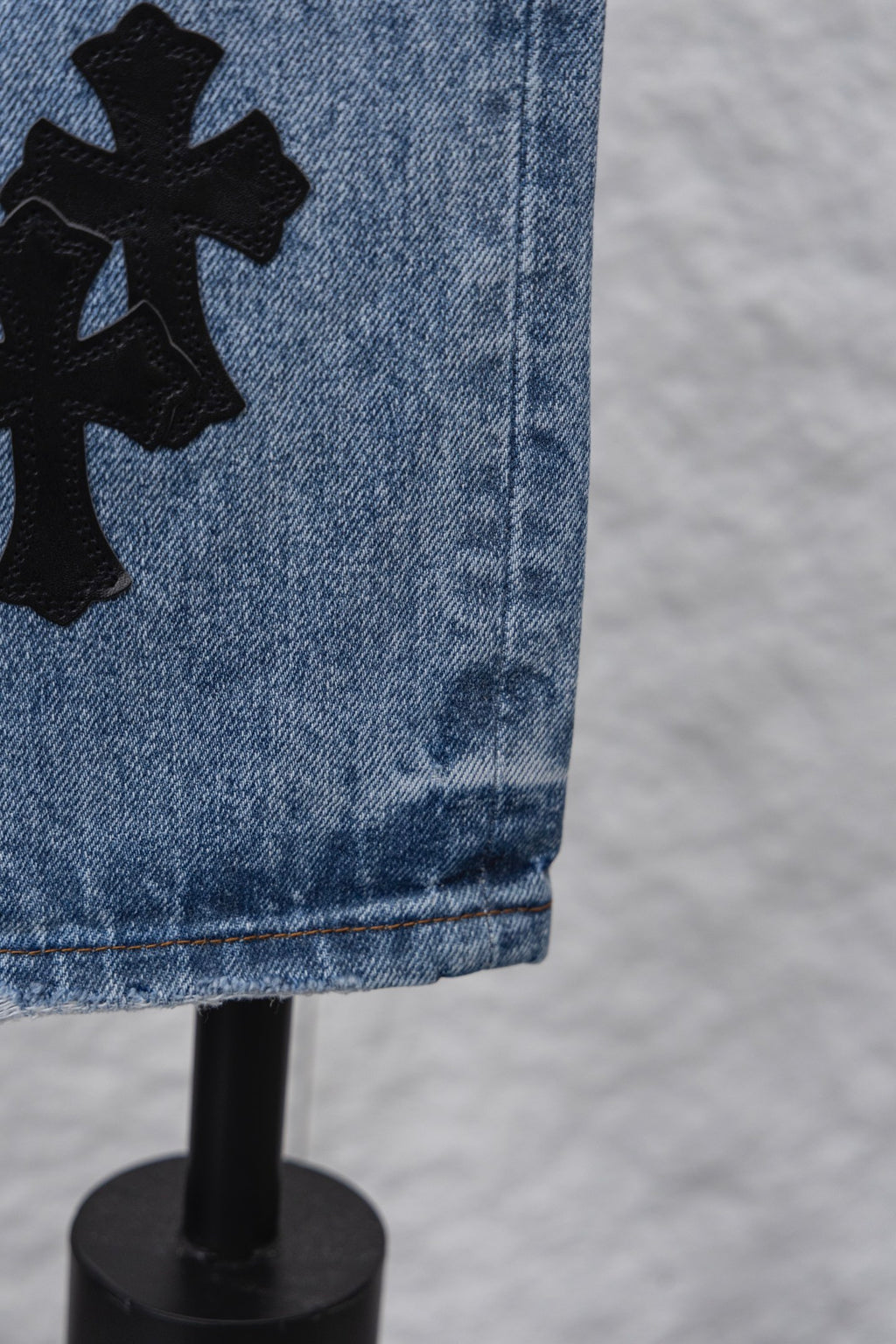 Light blue denim pants with large black cross patch on side, close-up.