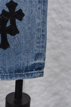 Light blue denim pants with large black cross patch on side, close-up.