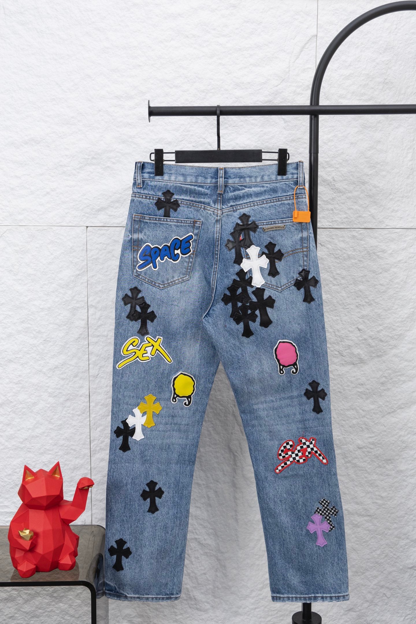 Light blue denim pants with multicolor graphic patches, front view.