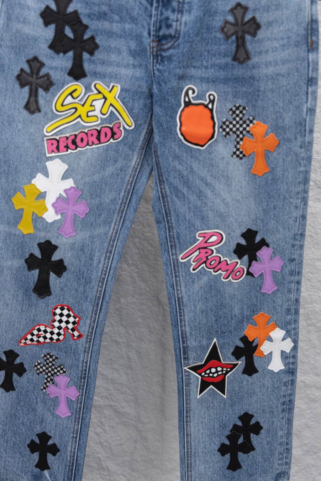 Light blue denim pants with colorful patch graphics, close-up.