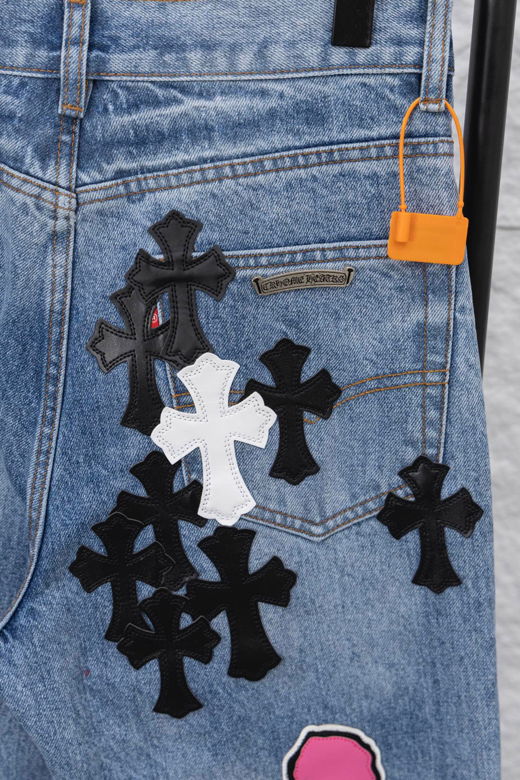 Light blue denim pants with black-and-white patch and orange tag, close-up.