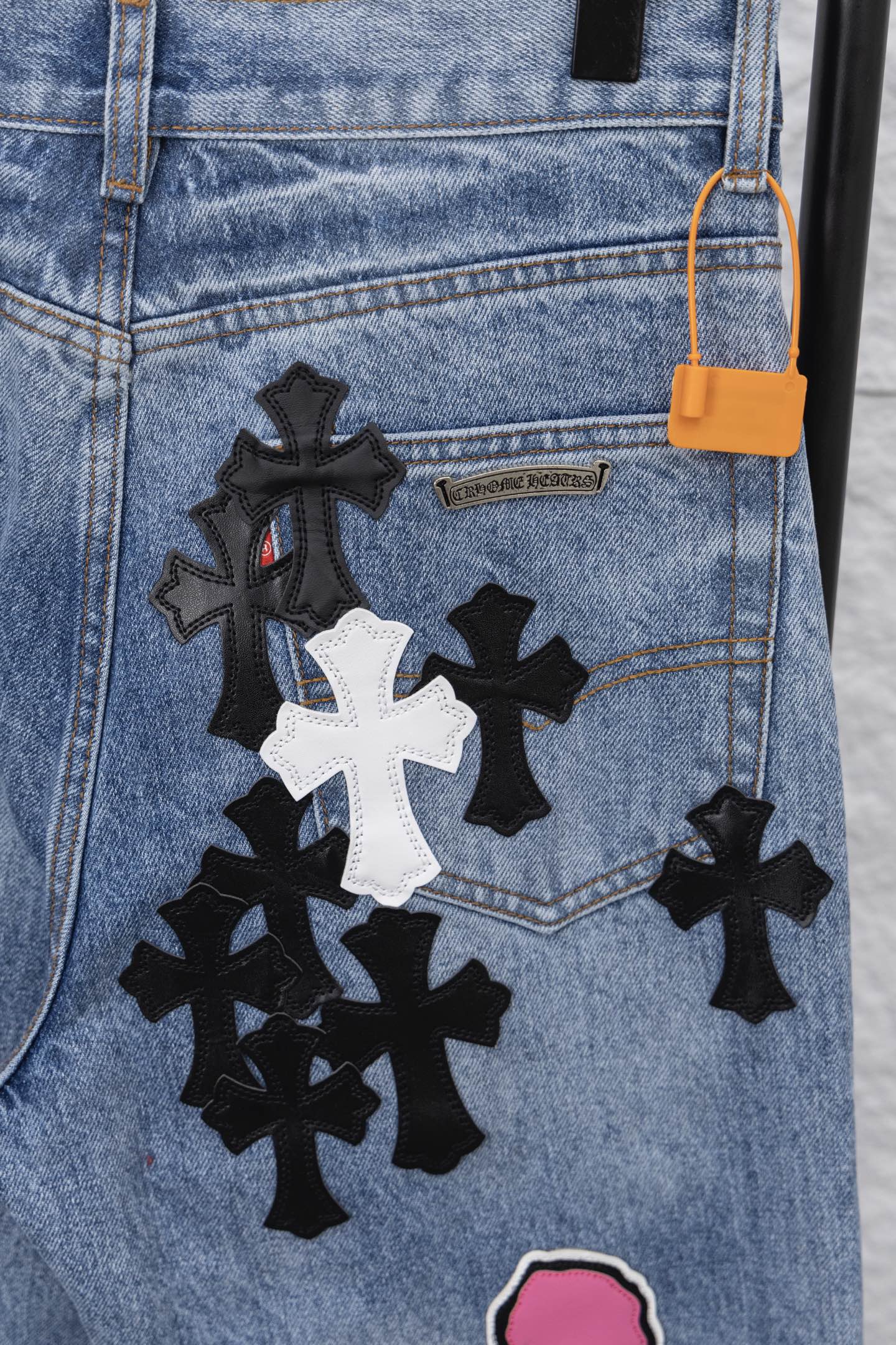 Light blue denim pants with black-and-white patch and orange tag, close-up.