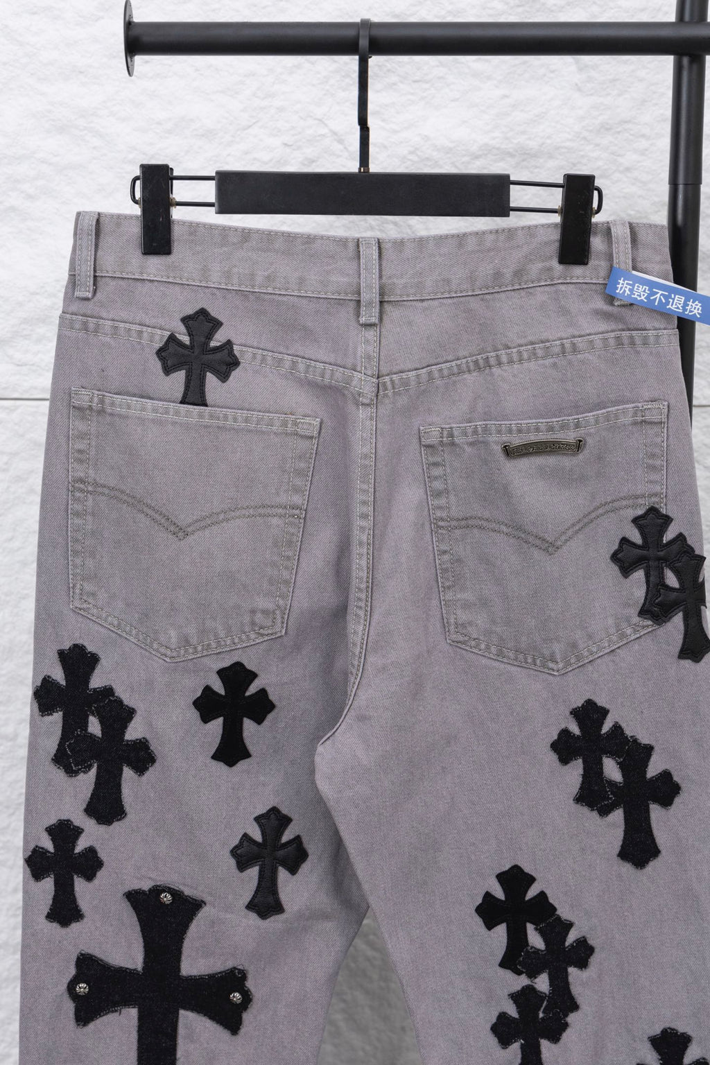 Light gray denim pants with black cross motifs on front pockets, close-up