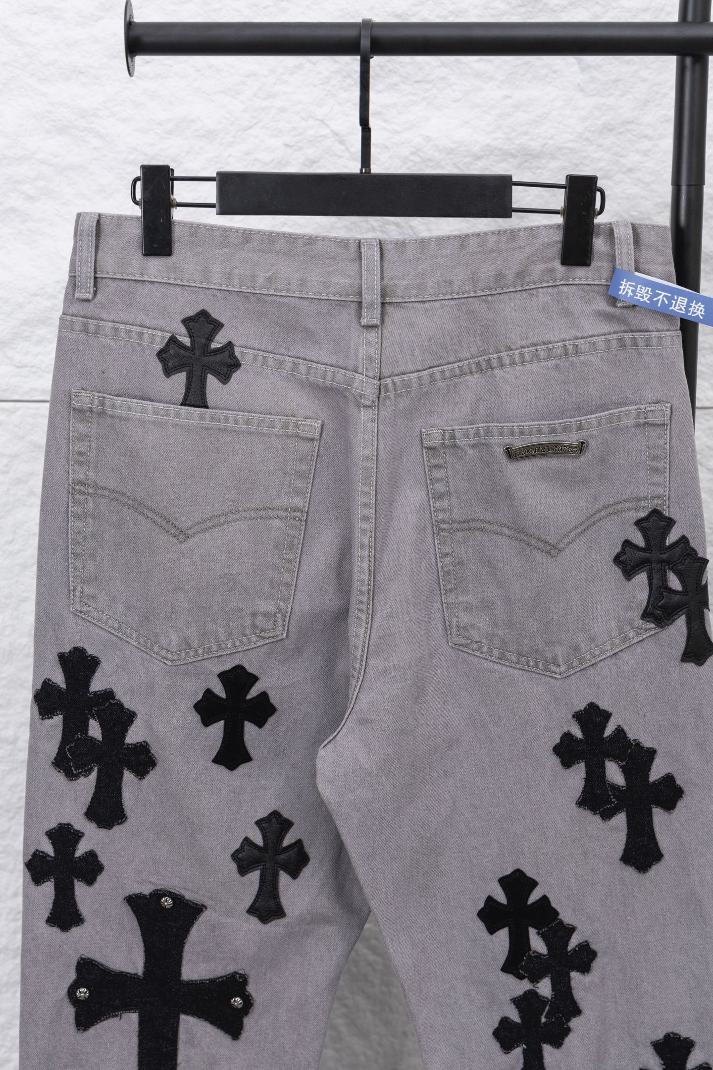 Light gray denim pants with black cross motifs on front pockets, close-up