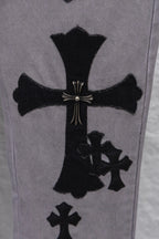 Light gray denim pants with large black cross applique and smaller cross motifs, close-up