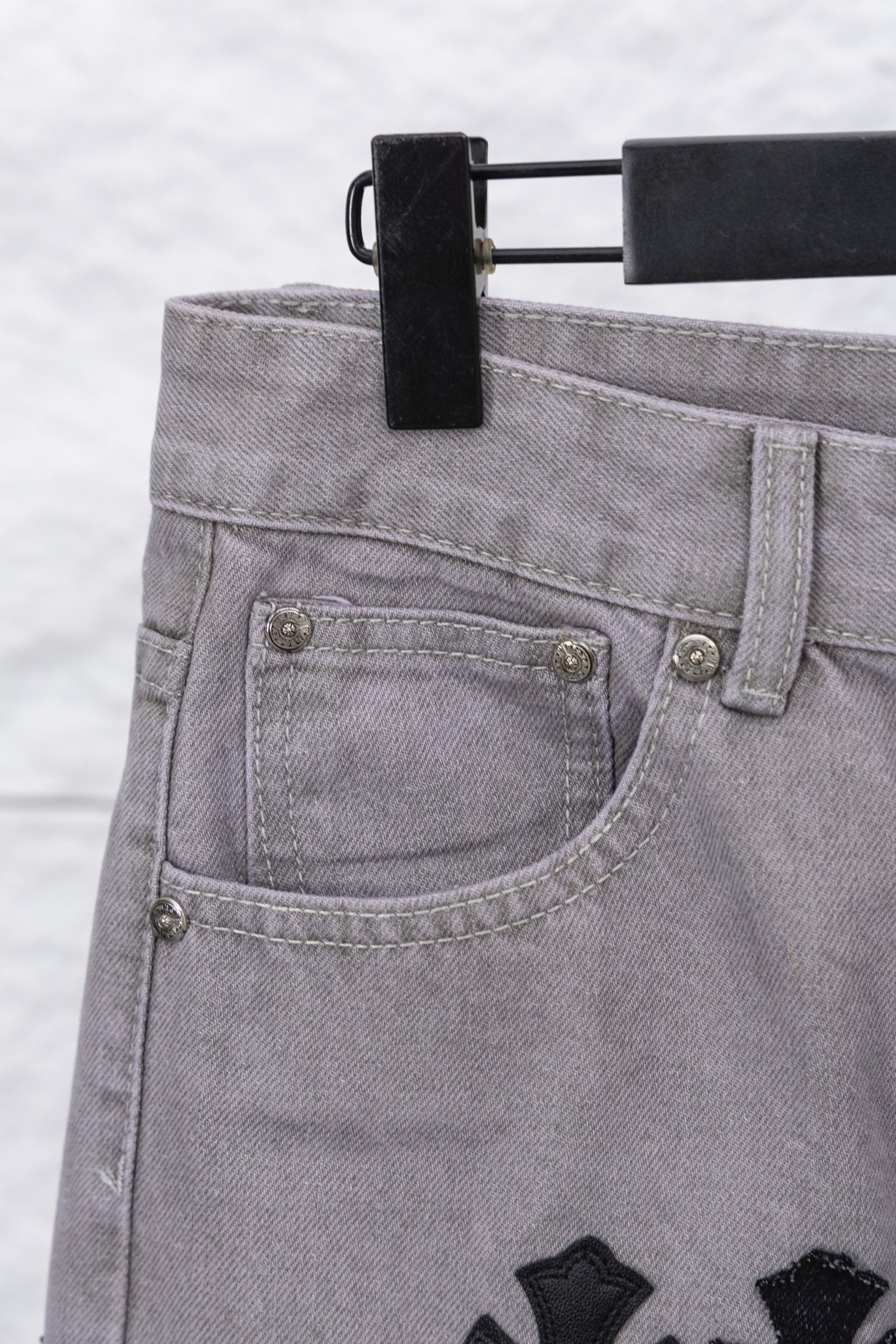 Light gray denim pants with curved front pocket and small metal buttons, close-up