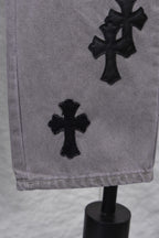 Light gray denim pants with black cross applique near hem, close-up