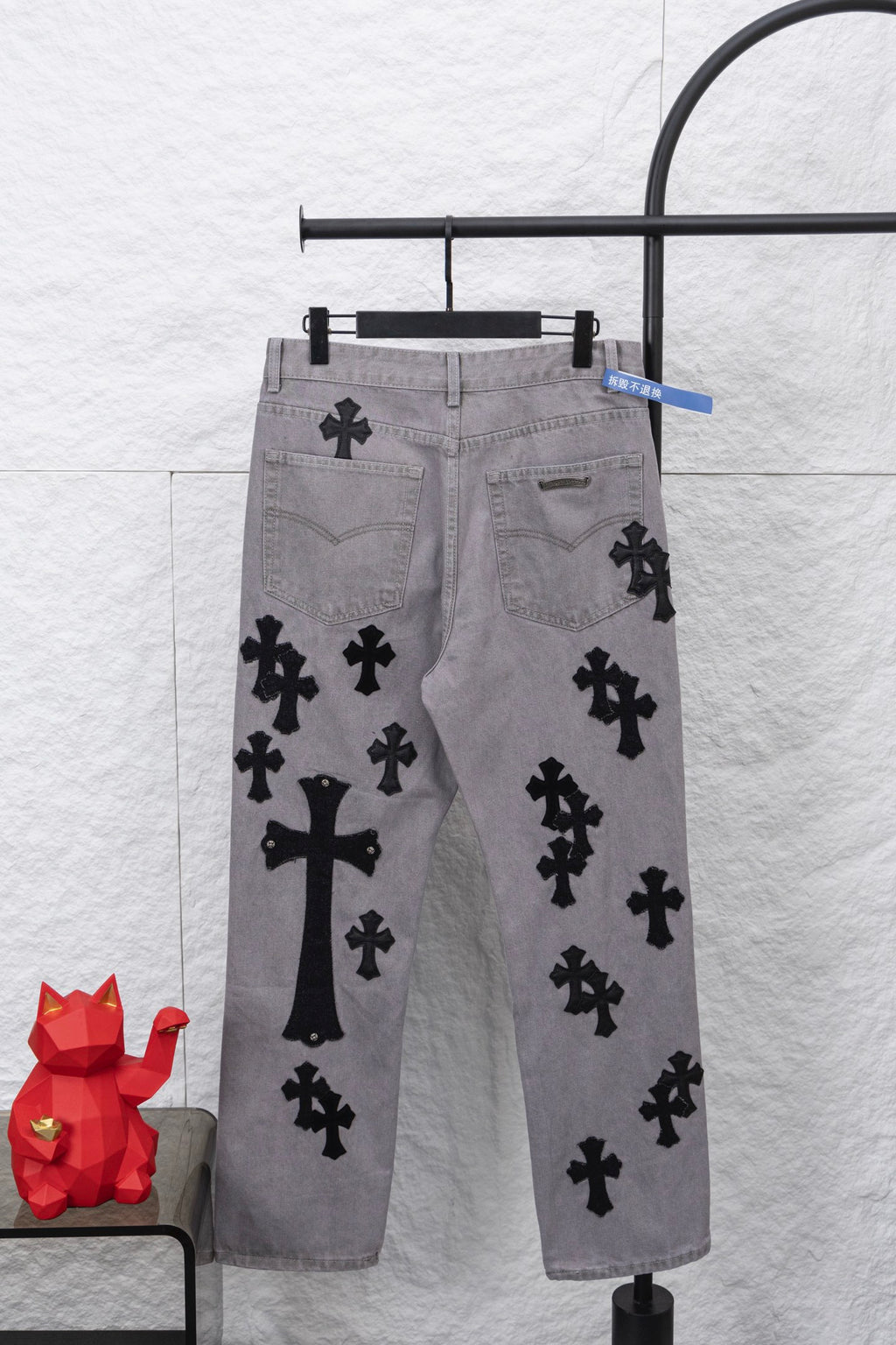 Light gray denim pants with black cross motifs and side pockets, front view