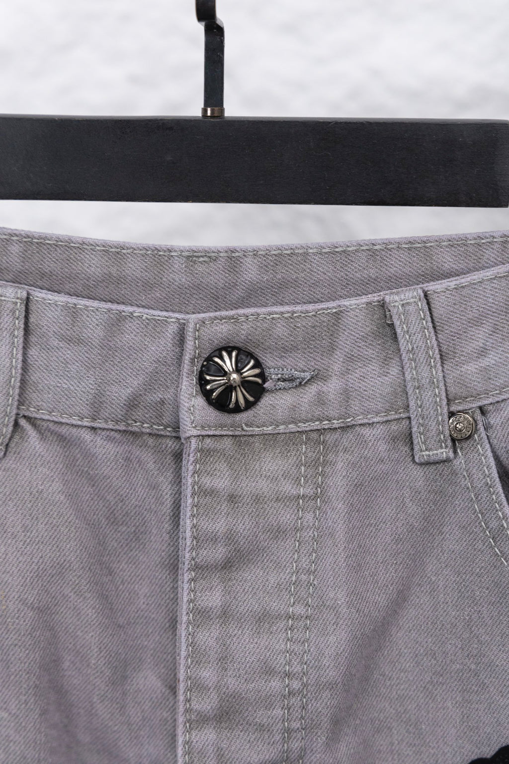 Light gray denim pants waistband with circular button and belt loops, close-up
