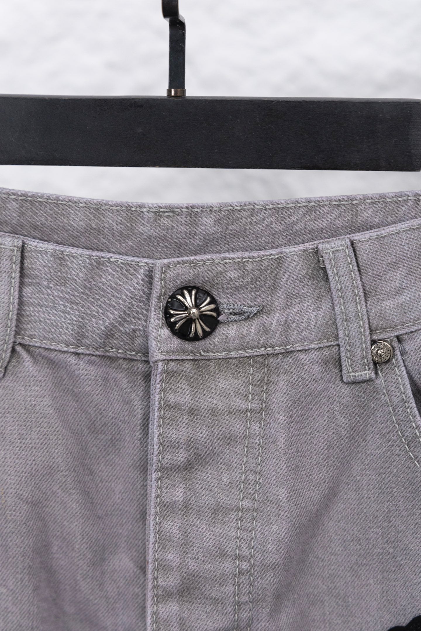 Light gray denim pants waistband with circular button and belt loops, close-up