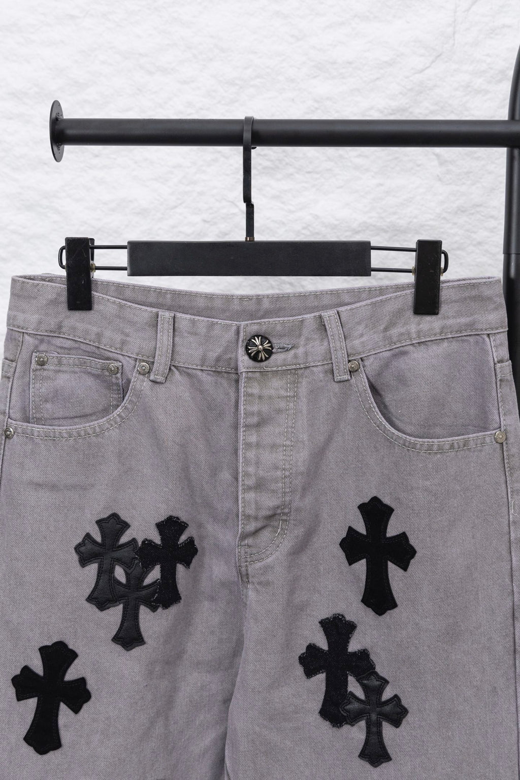 Light gray denim pants with black cross motifs across the legs, front view