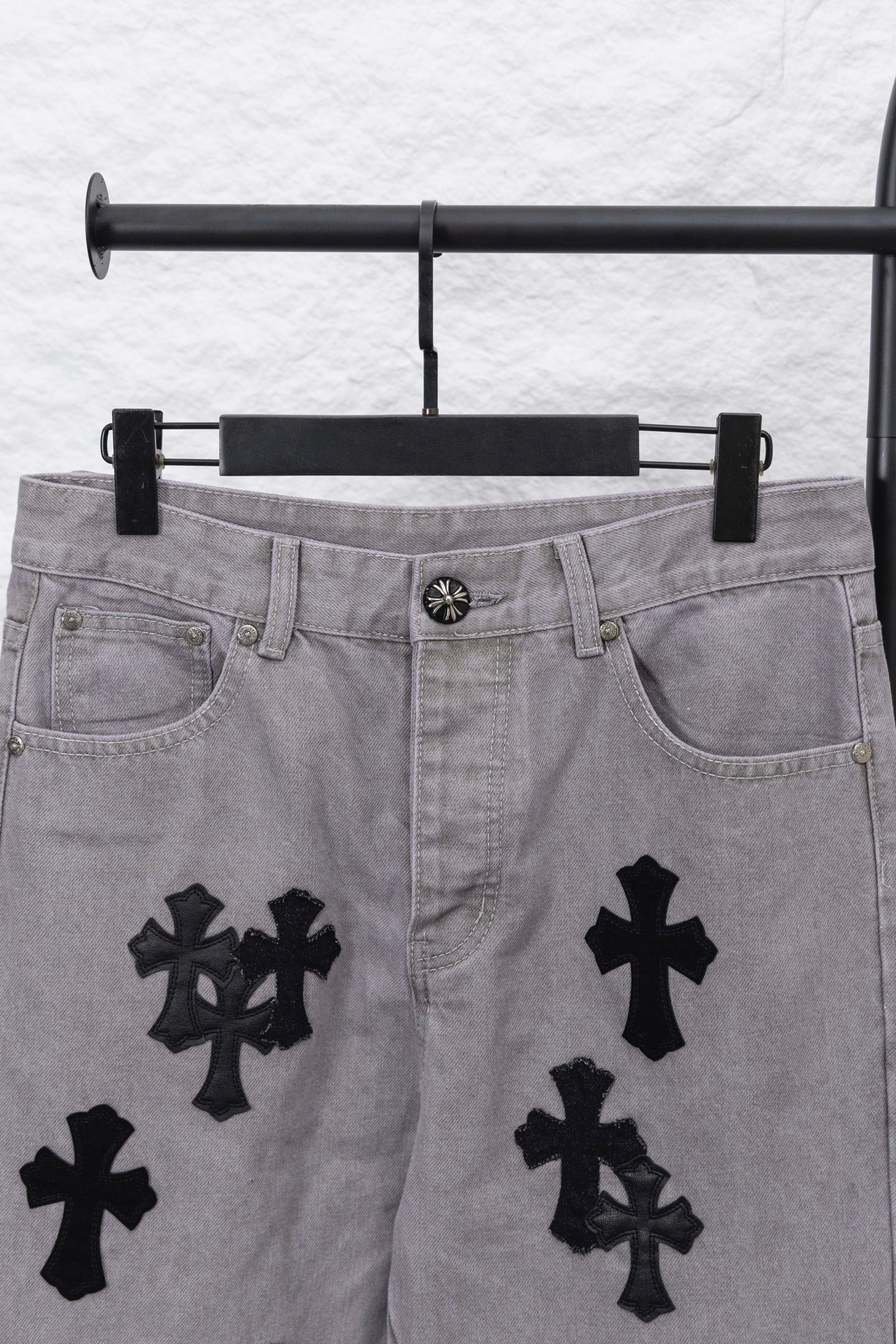 Light gray denim pants with black cross motifs across the legs, front view