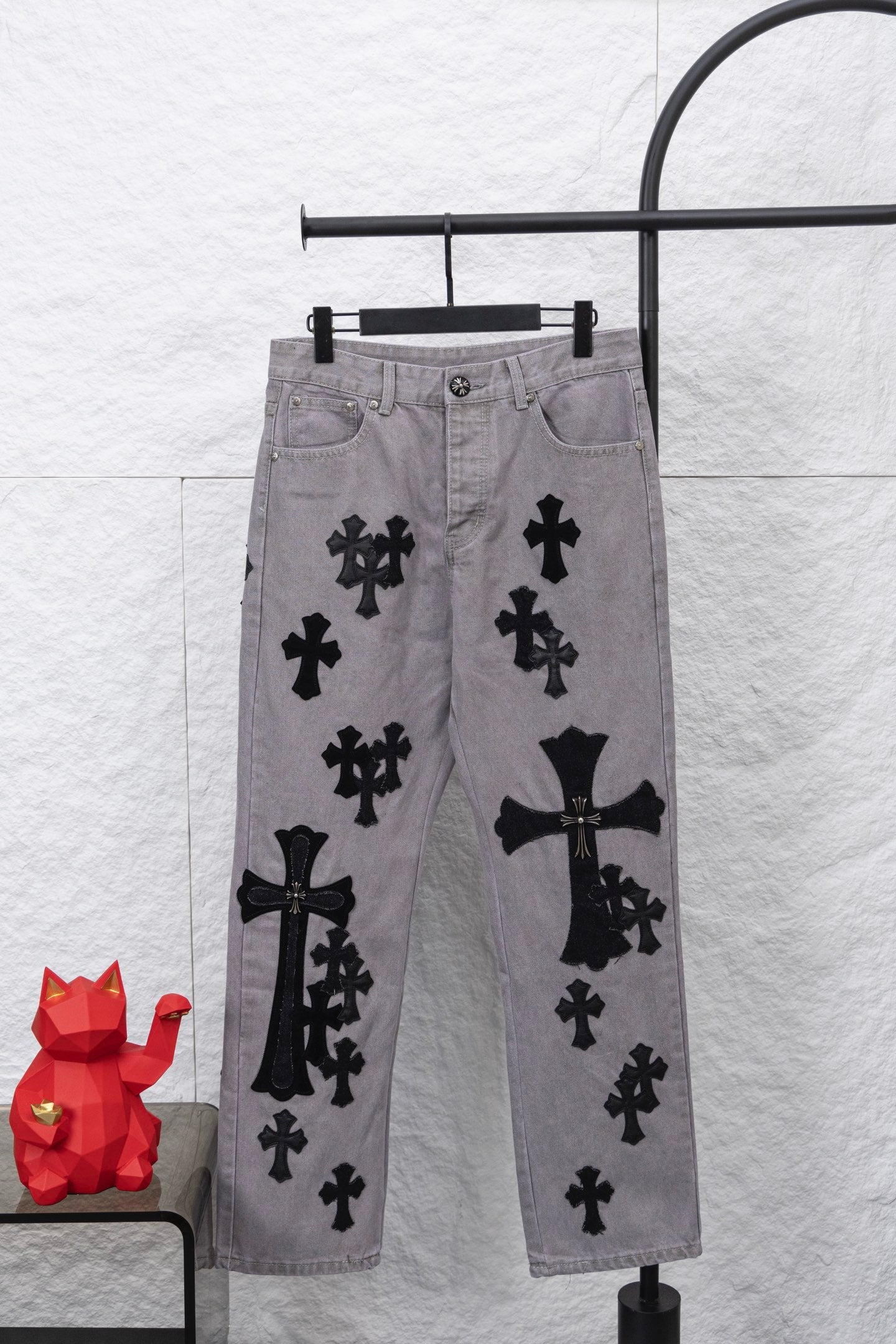 Light gray denim pants with black cross and bow-like appliques, front view