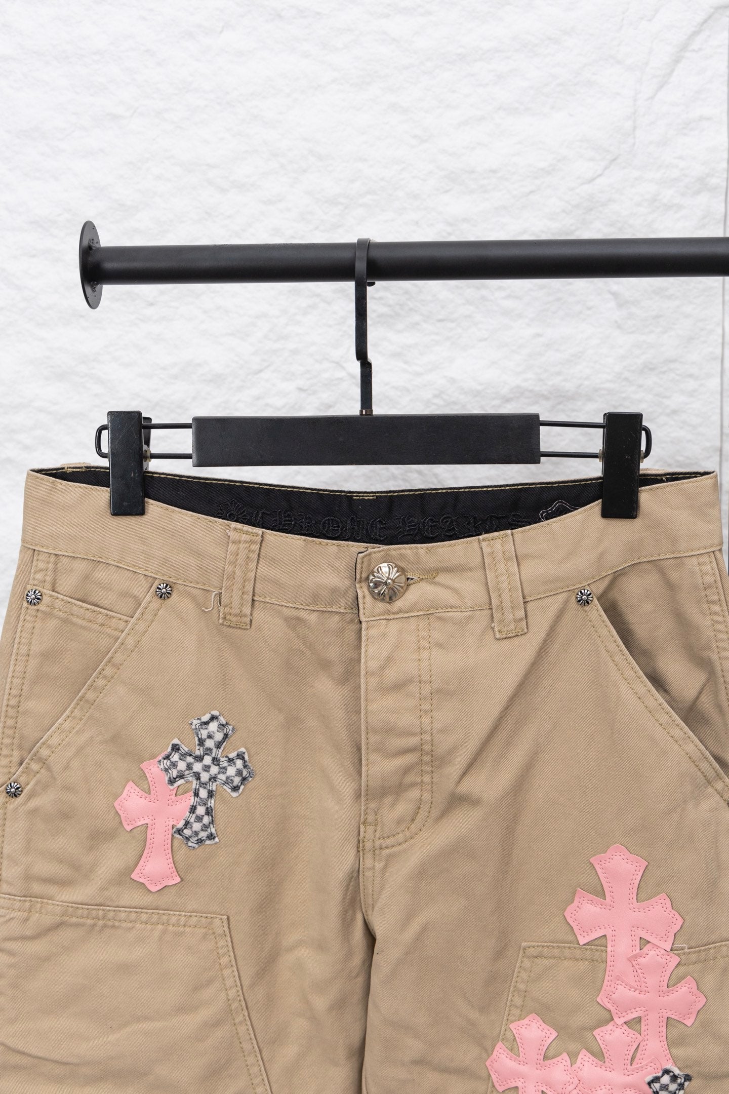 Tan pants front view with black inner waistband and pink and patterned cross patches