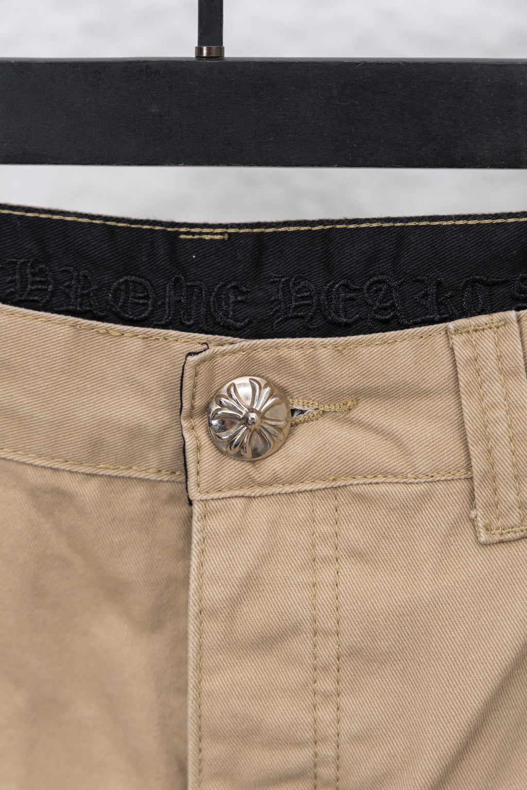 Tan pants button and waistband close-up with embossed brand detail
