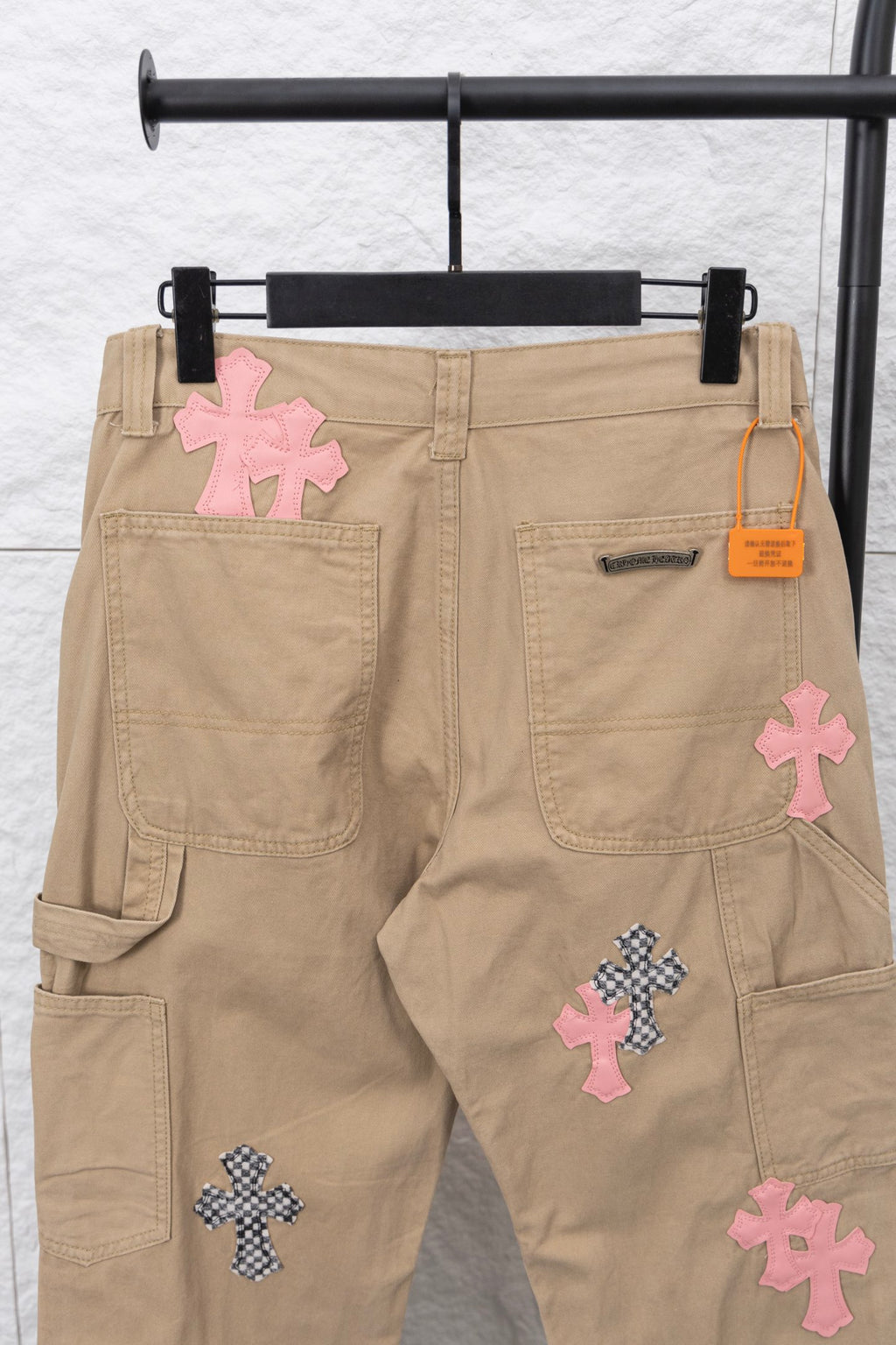 Beige cargo pants with cross appliqué patches and orange logo tag