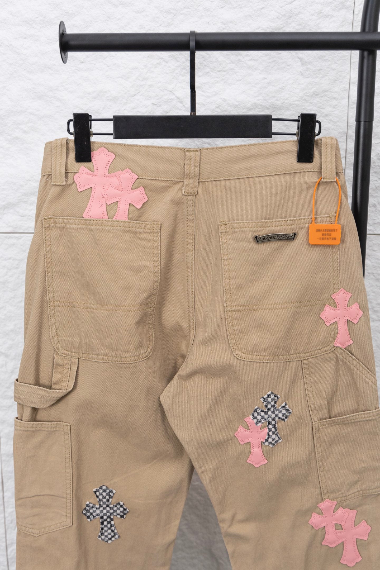 Beige cargo pants with cross appliqué patches and orange logo tag