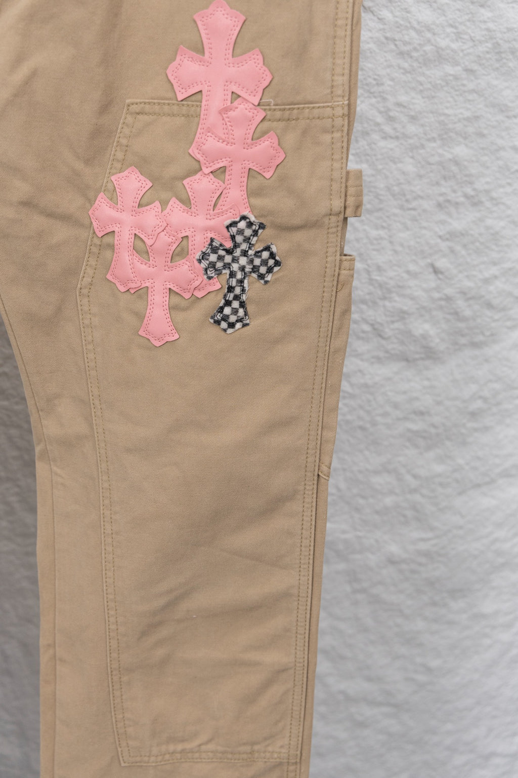 Tan pants leg close-up with pink cross appliques and small buttoned pocket