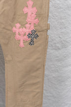 Tan pants leg close-up with pink cross appliques and small buttoned pocket