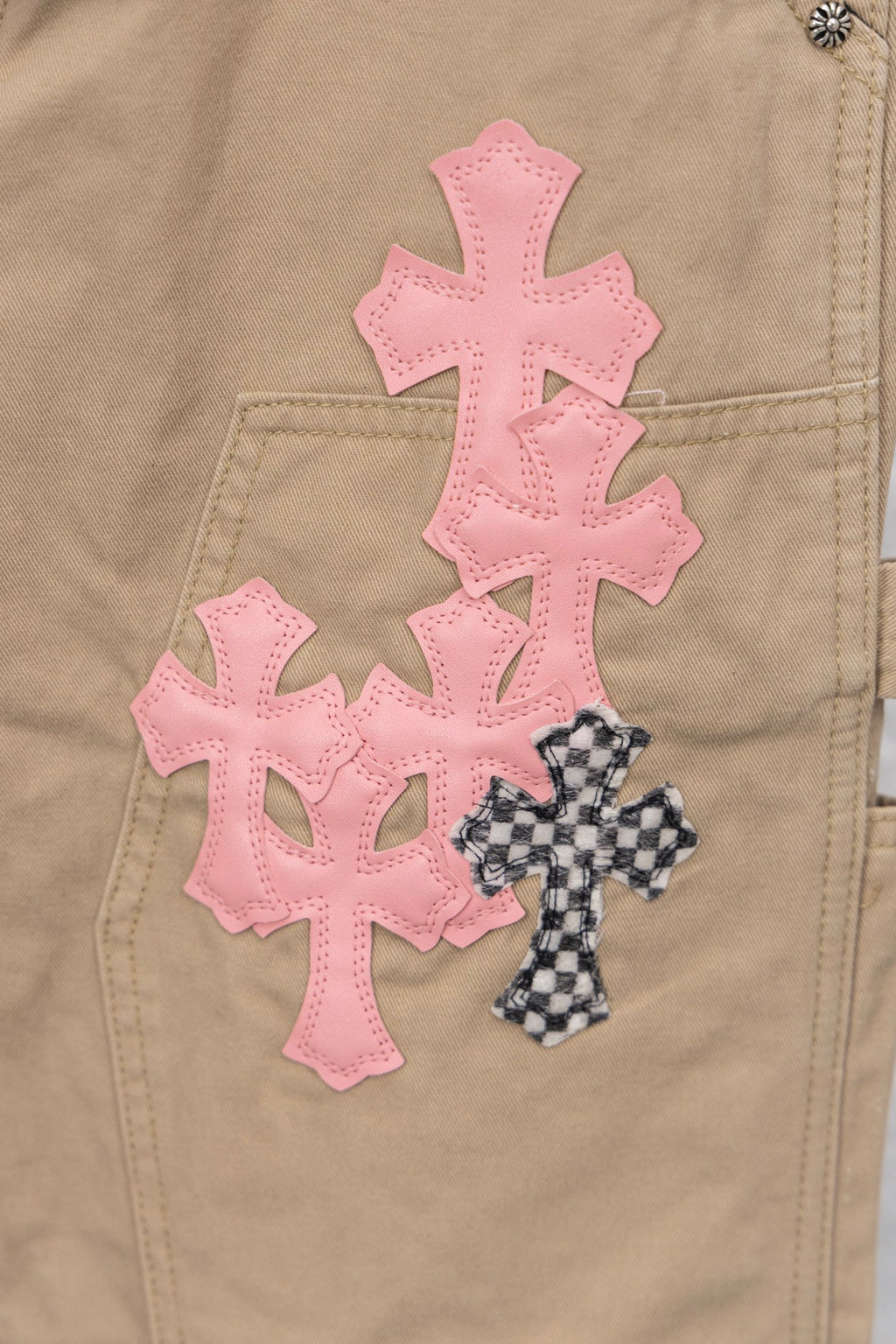 Tan pants close-up showing large pink cross appliques and a small patterned cross
