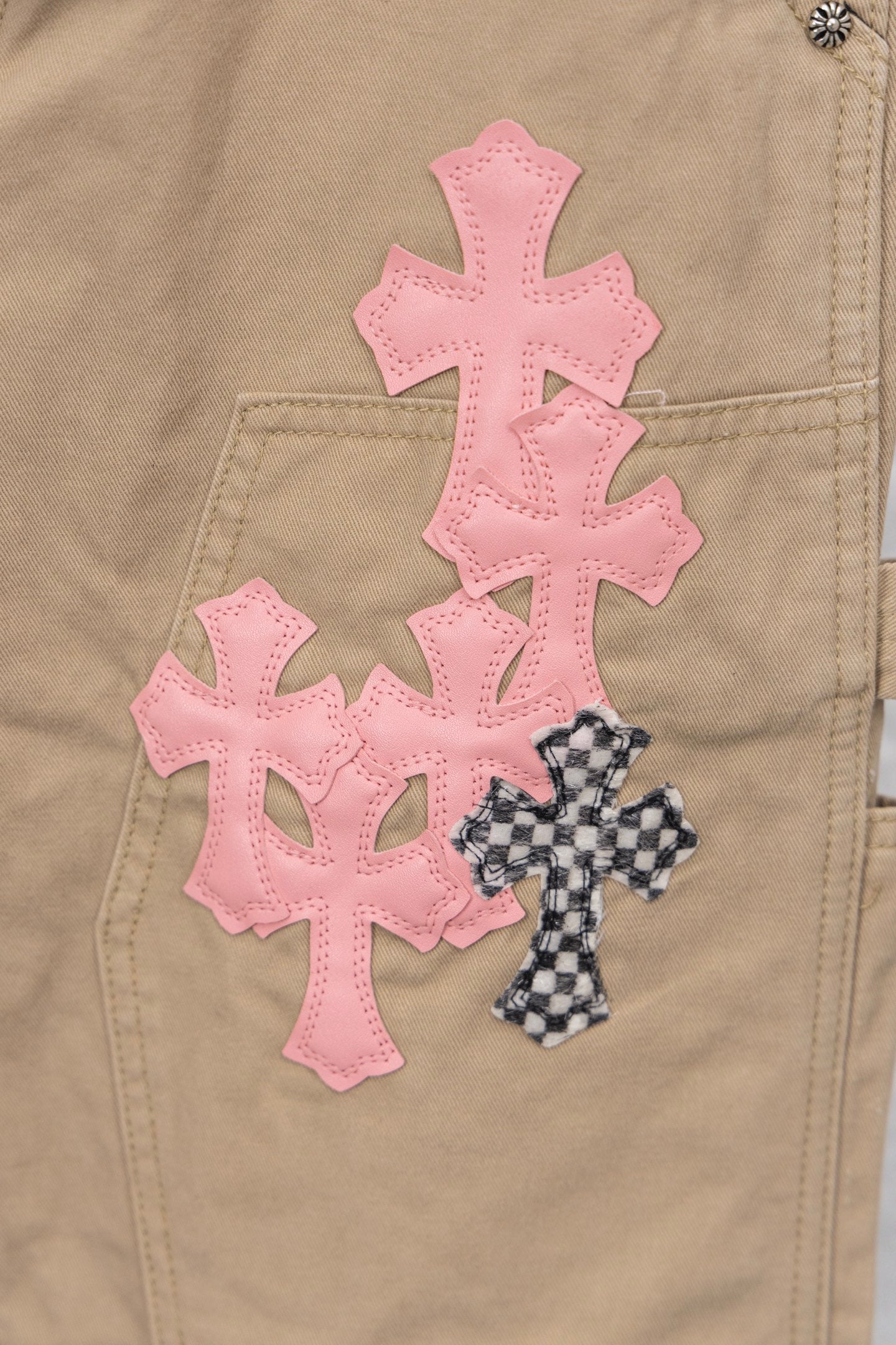 Tan pants close-up showing large pink cross appliques and a small patterned cross