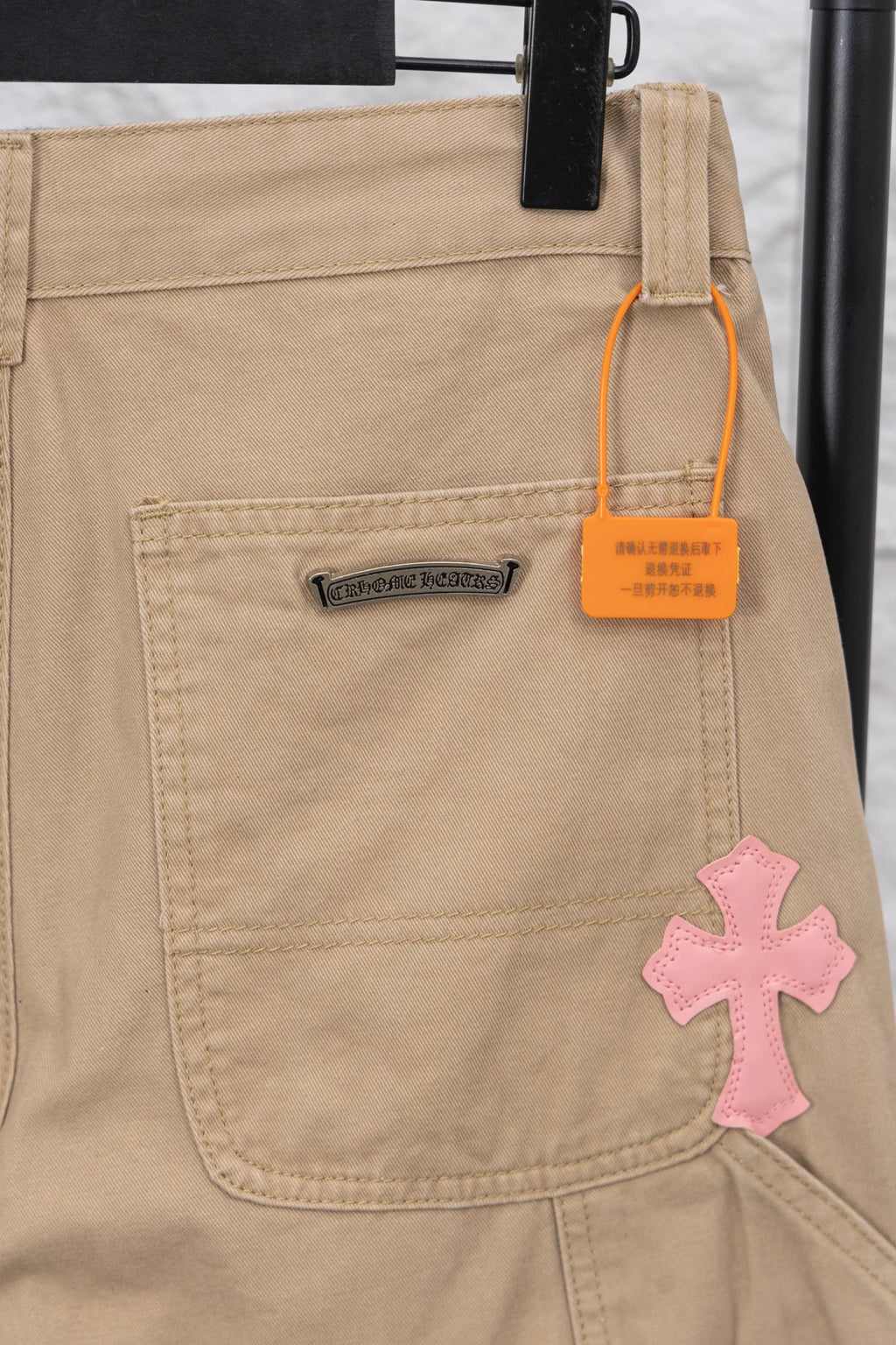 Tan pants front with cargo pocket, rectangular logo patch, and orange size tag