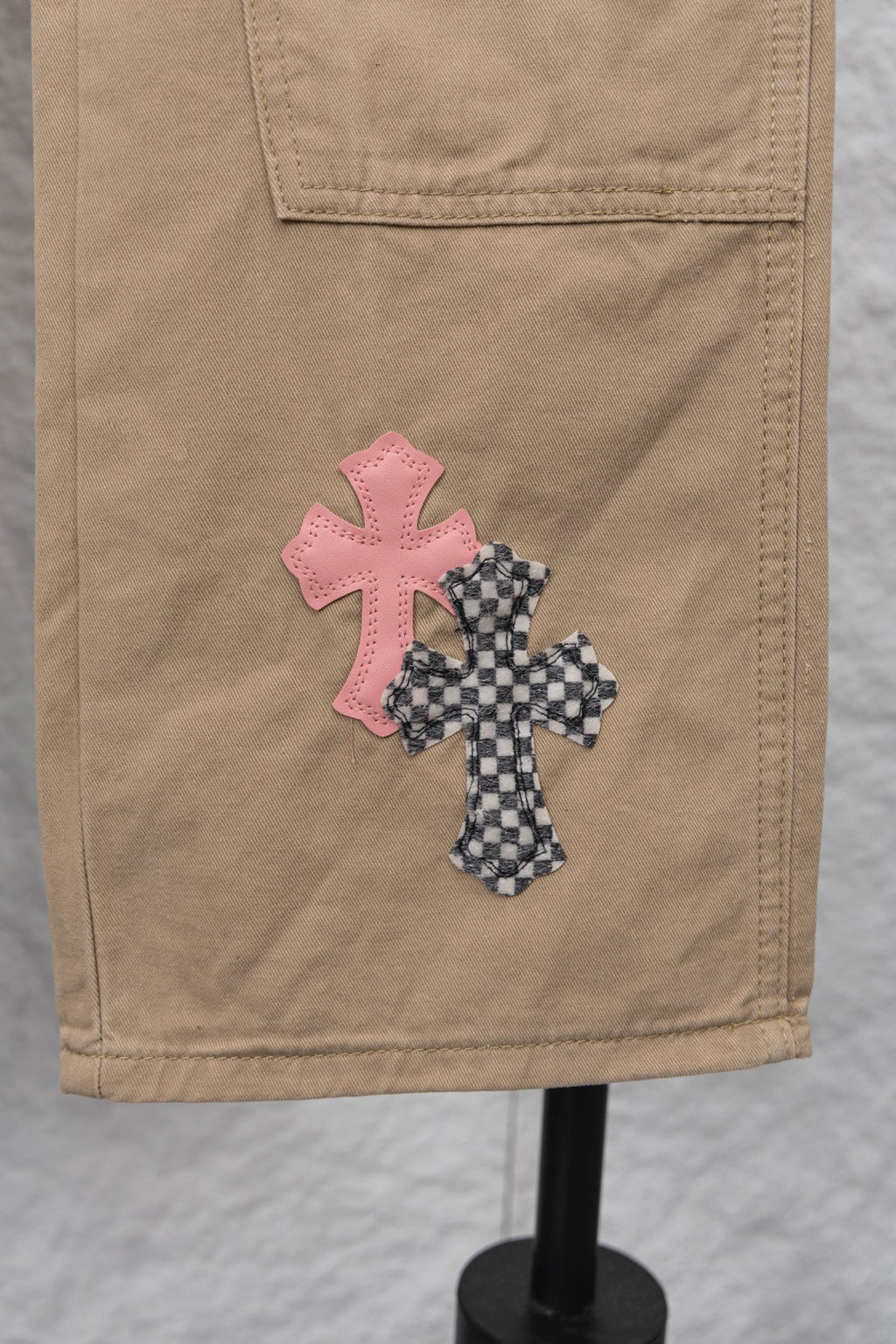 Tan pants with pink and patterned cross appliques on the front pocket area