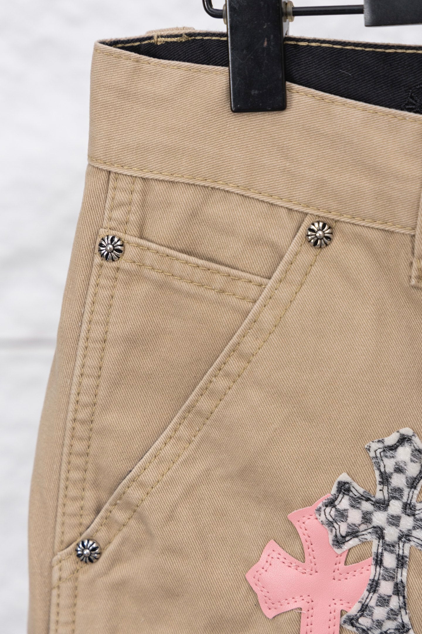 Tan pants close-up with metal button details and stitched diagonal seam