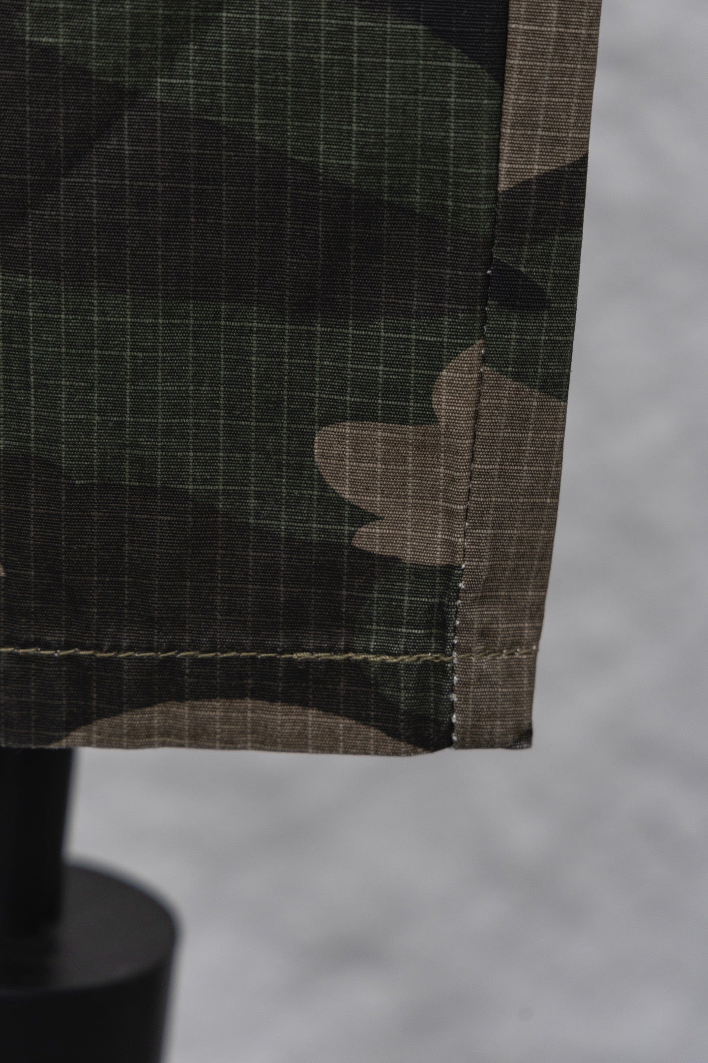 Hem and pocket edge of camouflage pants with dark stitching close-up