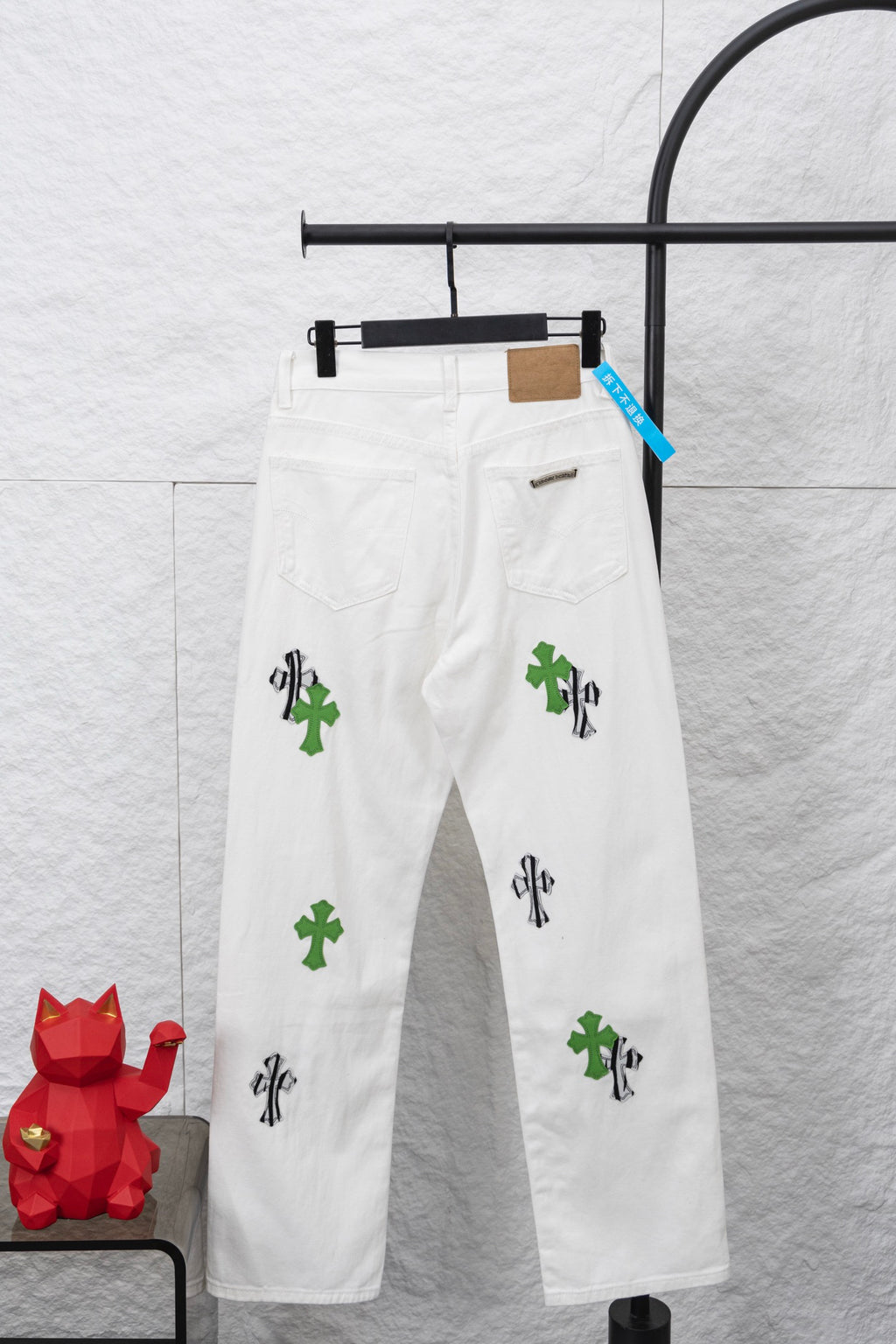 White denim pants with green and black cactus-style prints, front view on hanger
