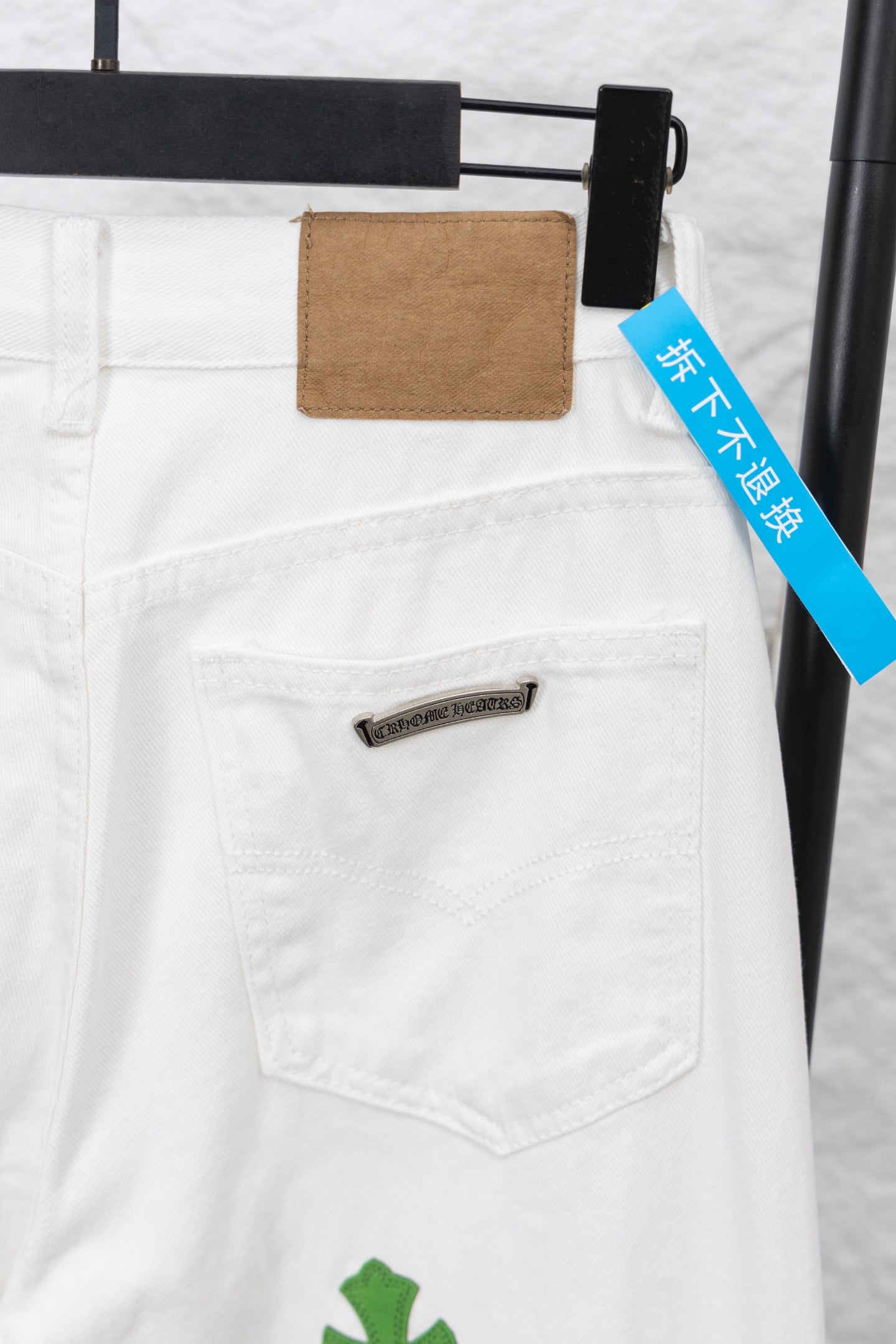 White denim pants back pocket with brown patch label and blue tag, close-up