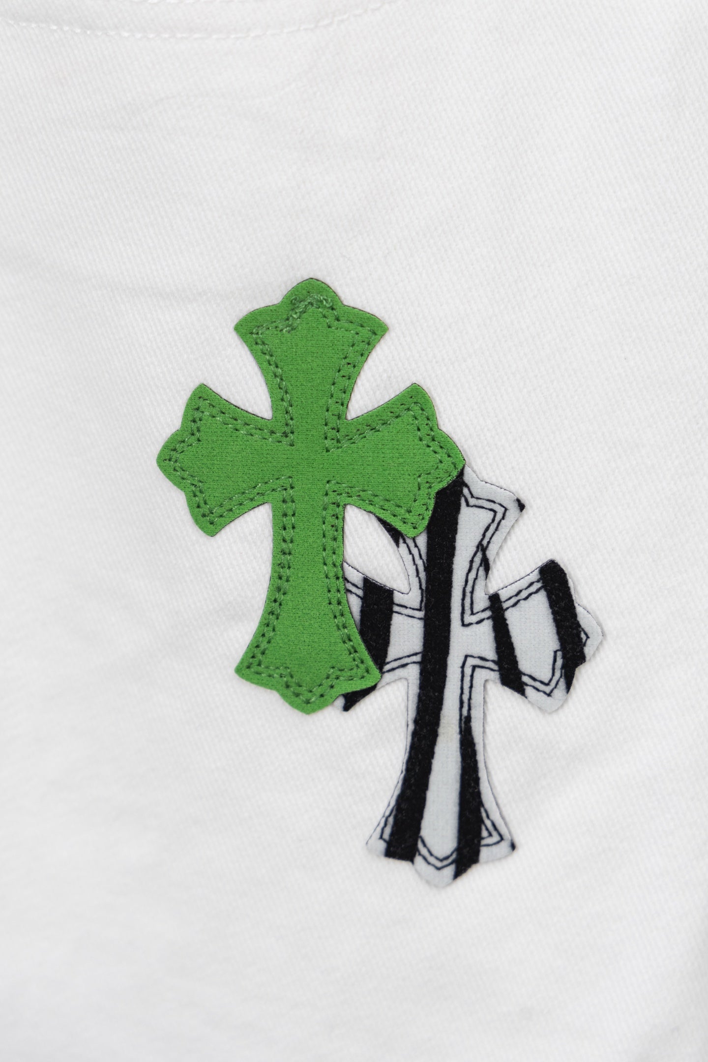 Green and black cactus-style patch graphic on white denim, close-up