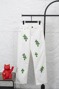 White denim pants with green and black cactus-style patches, front view on hanger