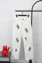 White denim pants with green and black cactus-style patches, front view on hanger
