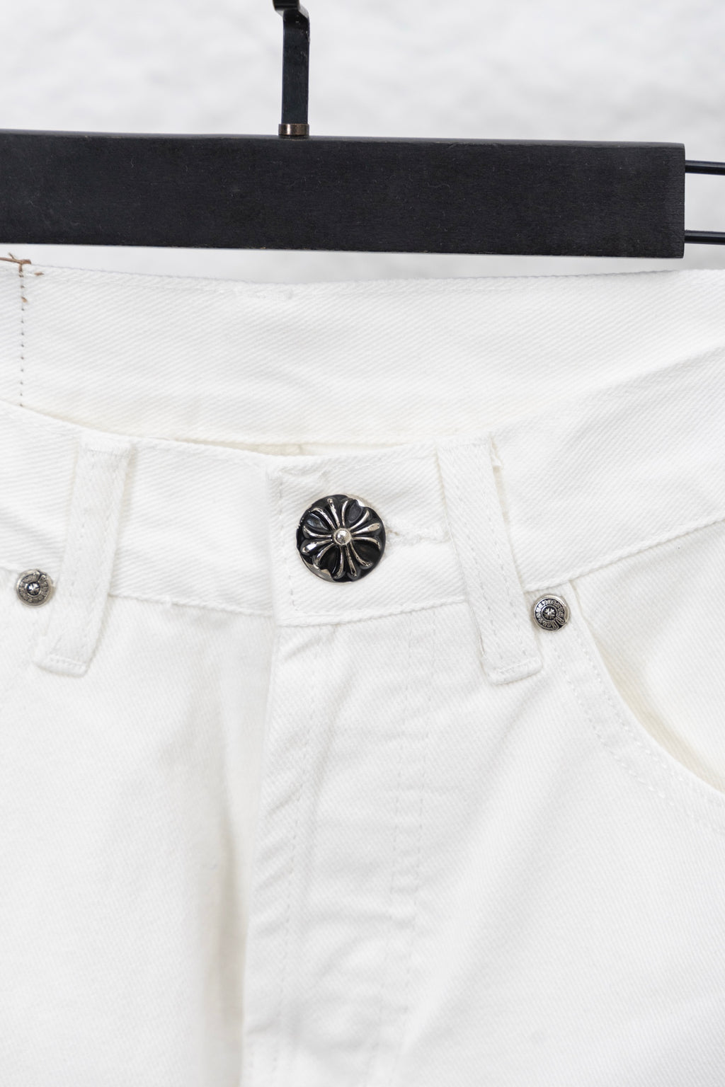 White denim pants waistband and button closure with round emblem, close-up