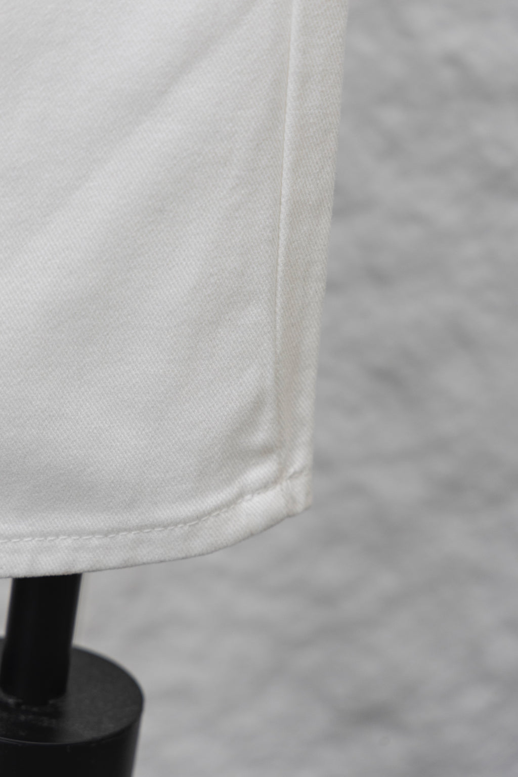 White denim pant leg with visible seam and bottom edge, close-up